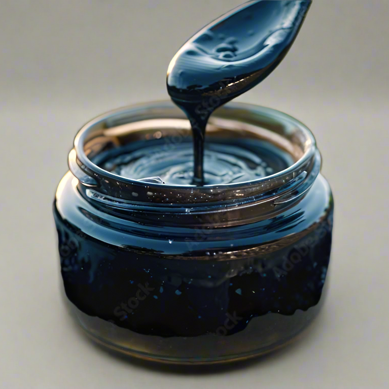 Jar of dark blue gel with a spoon dripping into it on a light gray background